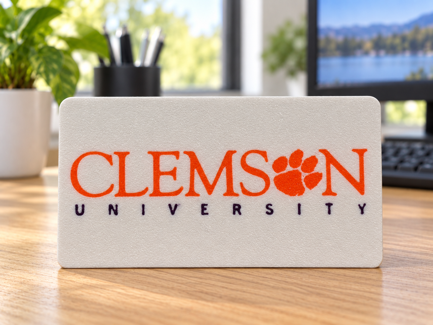 White plaque with orange CLEMSON lettering and paw, and purple UNIVERSITY lettering standing on an office desk